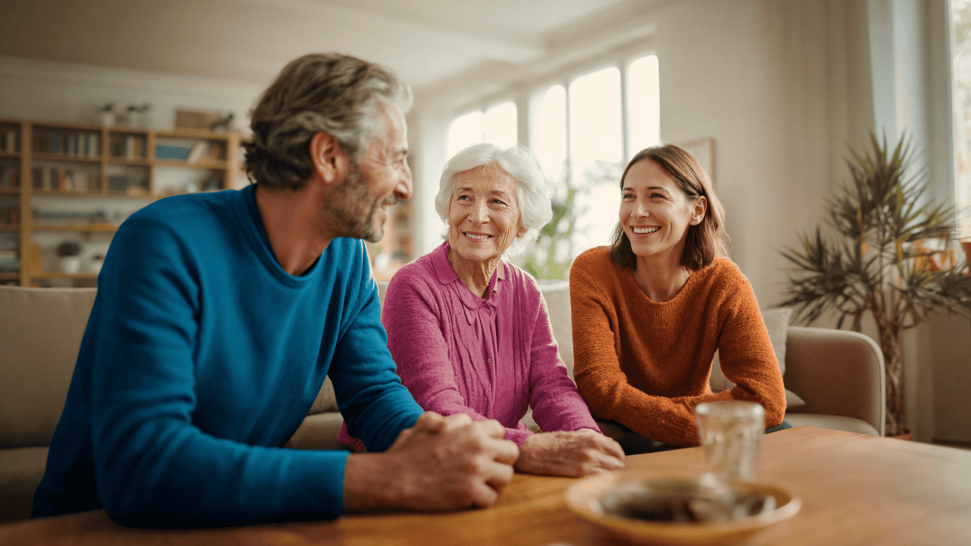 Happy elderly woman sitting at home with her adult children, representing Live-in Care as an alternative to nursing home.